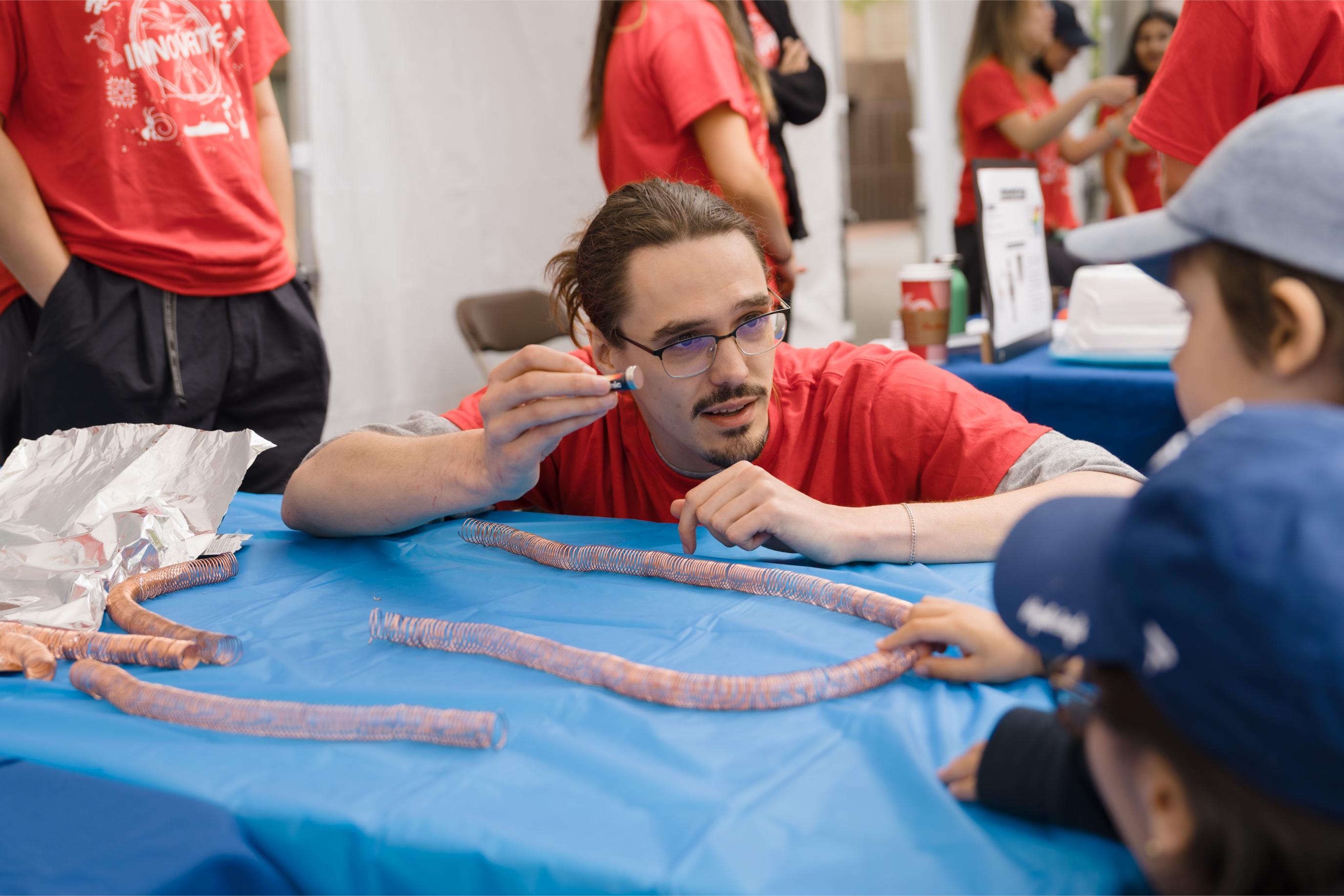 A volunteer engaging with participants at the Fun with Physics Booth.